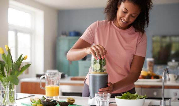 Woman preparing a healthy smoothie in a kitchen blender.