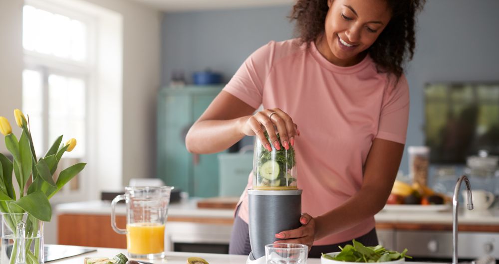 Woman preparing a healthy smoothie in a kitchen blender.