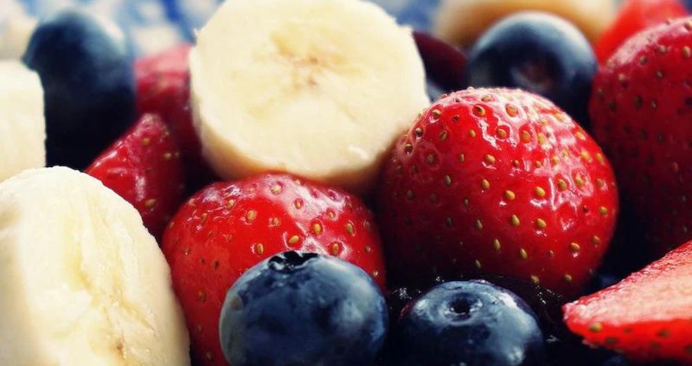 a close up picture shows bananas, blue berries and strawberries