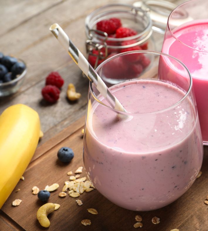 a cup of berry smoothie with bananas, red and blue berries around the cup